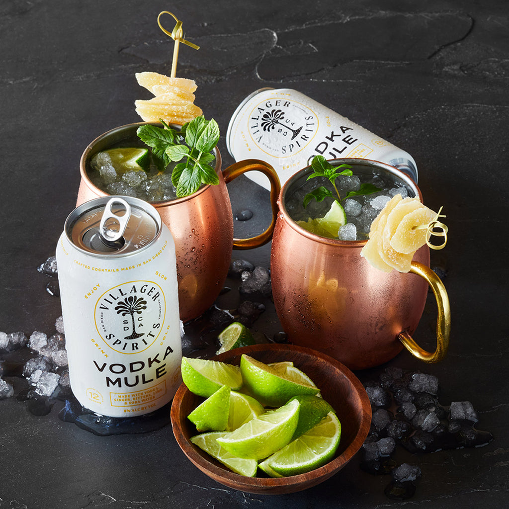 Two freshly made Villager Spirits Vodka Mule cocktails in tin mugs garnished with candied ginger, mint and lime.